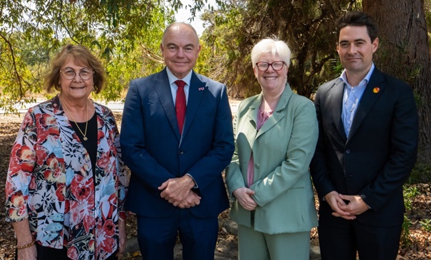 Four people standing looking towards camera with bushes in background