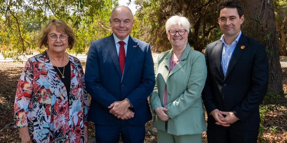 Four people standing looking towards camera with bushes in background