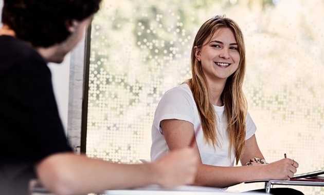 Student sits at desk and smiles at classmate