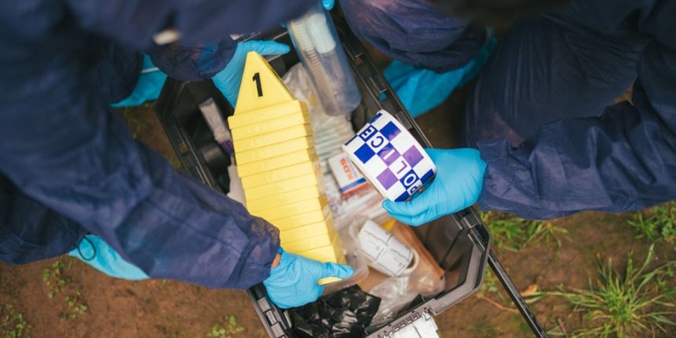 Two people in forensic gear taking tape and markers from a box.